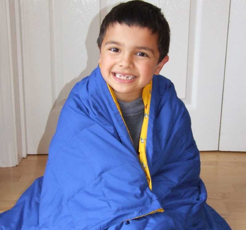 Smiling boy pulls a bright blue weighted blanket around him