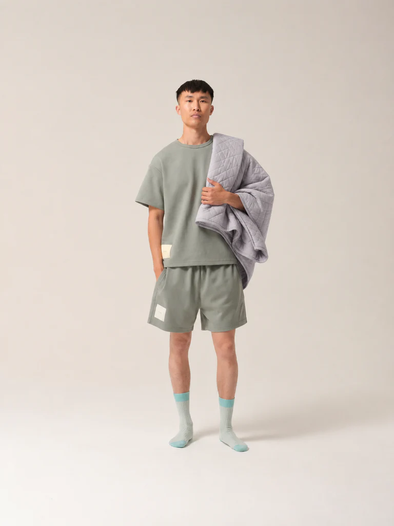 Man wears matching shorts and t shirt and carries a quilted grey blanket