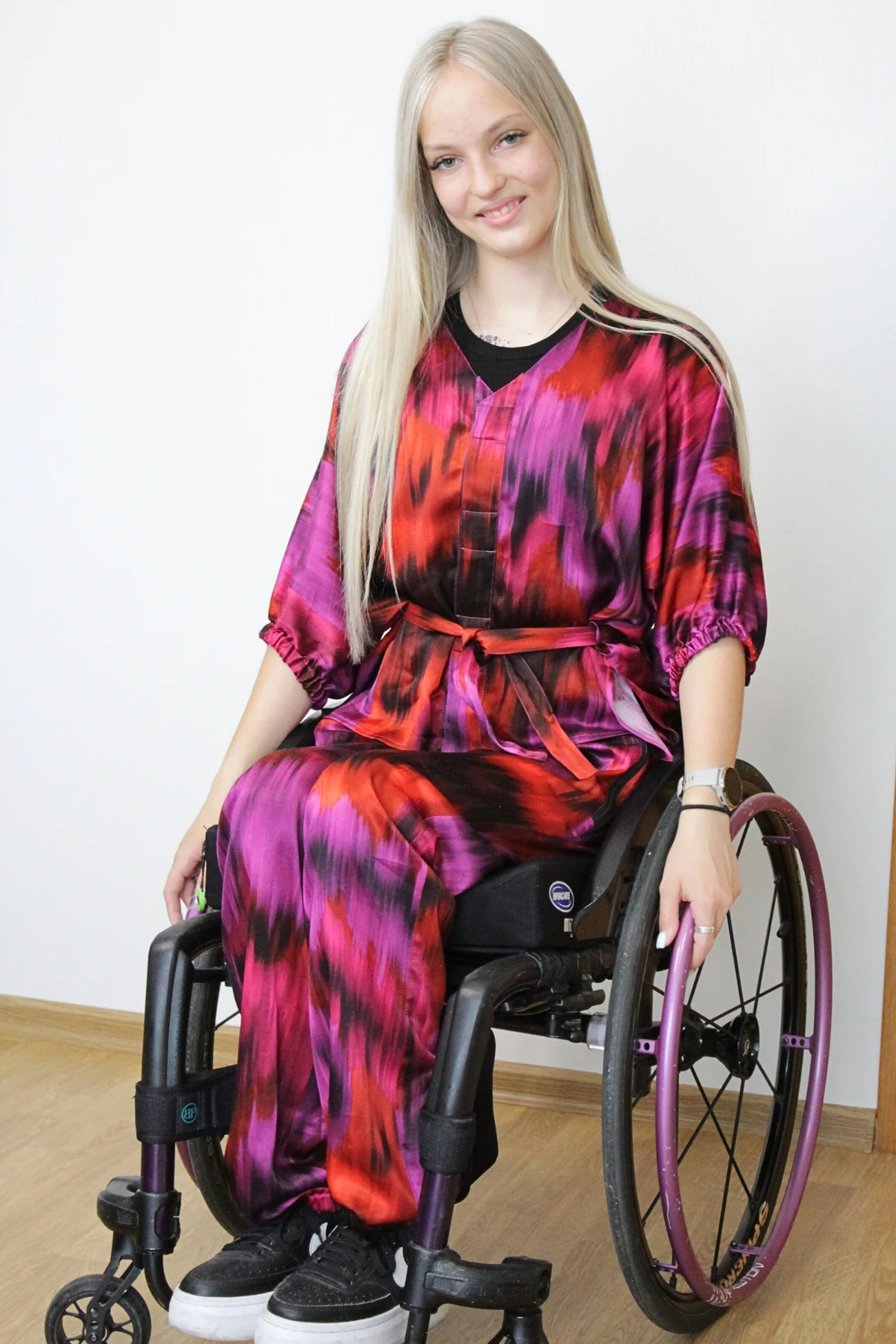 Woman wears adaptive blouse in a red and pink batik fabric top with magnetic closures and matching satin trousers