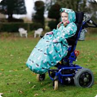 a child in a wheelchair, looking warm in a blue seagull theme wheelchair cosy cover and matching coat with hood