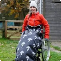 A teenage girl in a wheelchair with storm clouds and lightning theme wheelchair cosy cover, and red top.