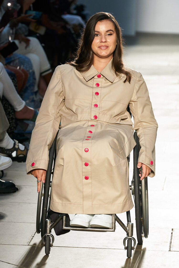 Woman using a wheelchair wears full length beige coat with red buttons