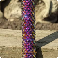 Purple bejewelled walking stick shown in close up against wood and stone