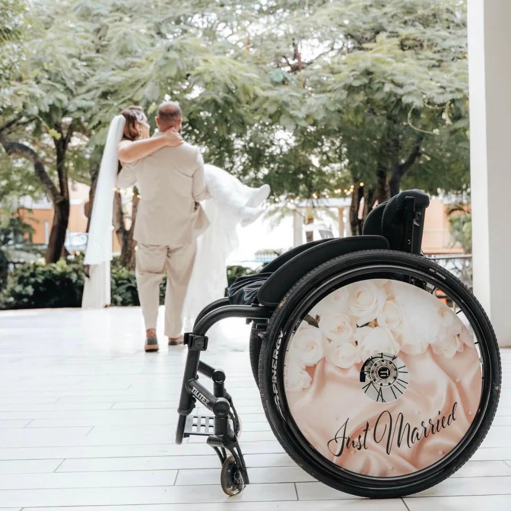 Bride is carried from wheelchair showing elegant pale pink design and Just Married in scroll font