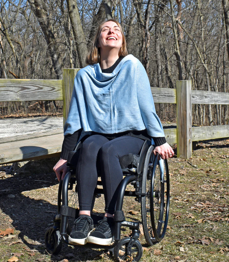 Woman in wheelchair smiles facing the sun wearing pale blue shawl