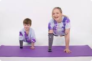 Woman and boy wearing purple and white t shirts are positioned to do press ups sharing a purple yoga mat and both have a right arm prosthetic