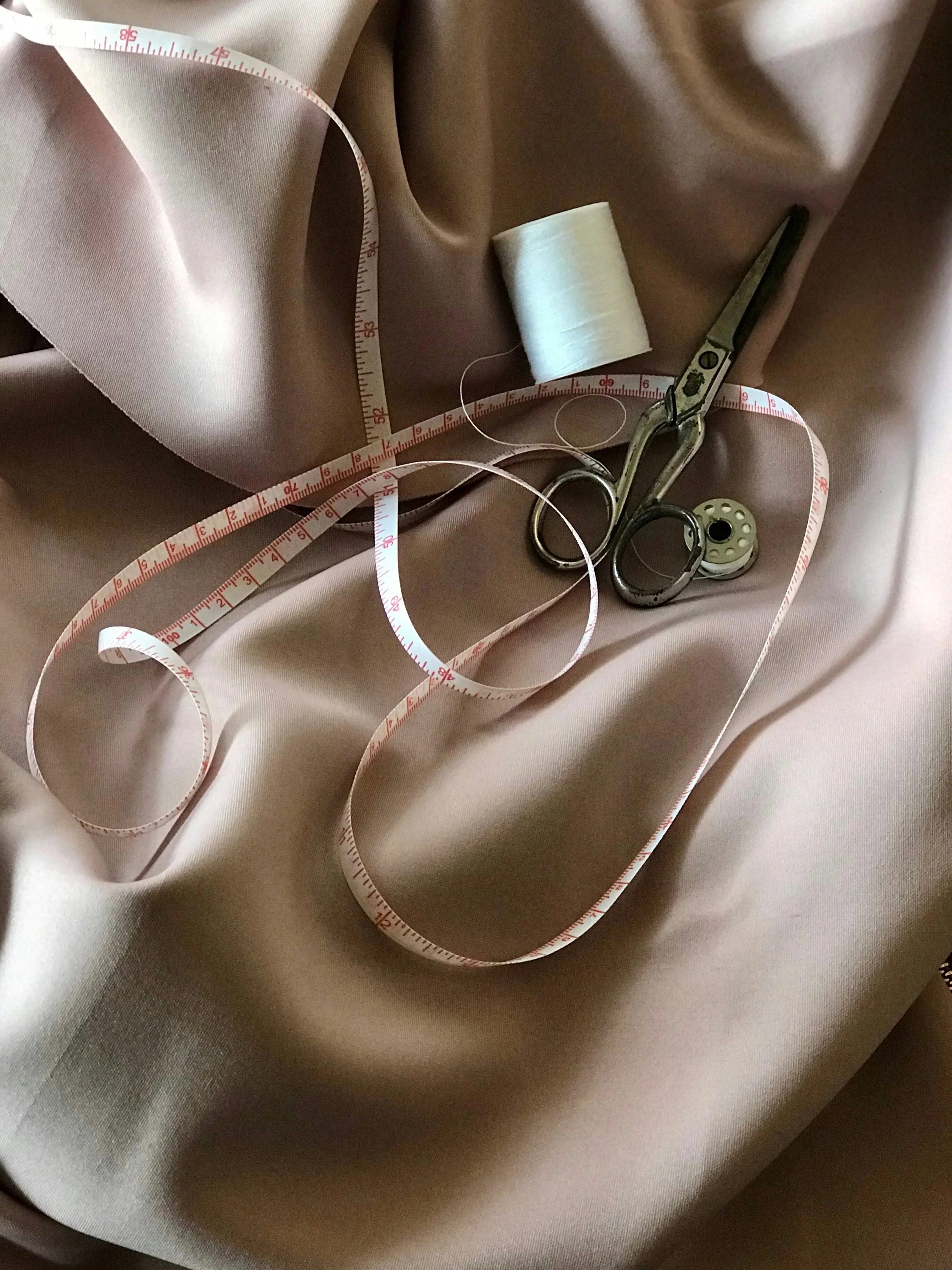 Tape measure, siccros and cotton reel are surrunded by beige silky fabrics